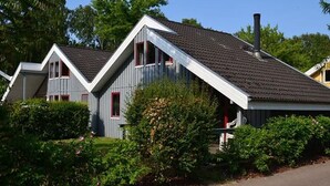 Uma fileira de casas modernas com telhados inclinados e molduras de janelas vermelhas, rodeada por vegetação bem cuidada.