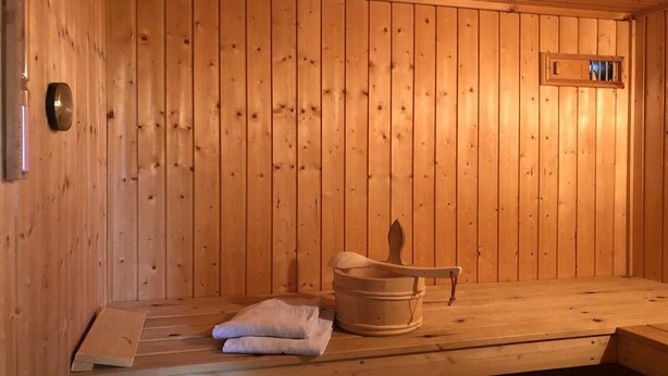 Uma sala de sauna de madeira com um banco, um balde de madeira e uma toalha.
