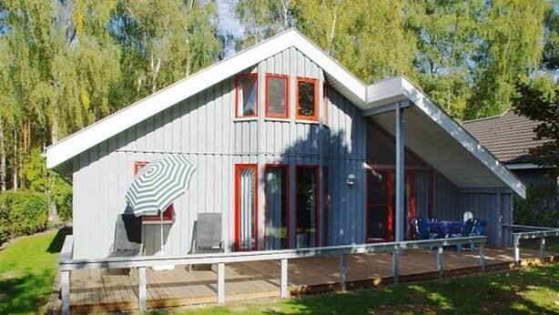 Una cabaña moderna con terraza, ventanas amplias y una puerta roja.