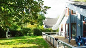 Una casa moderna con una terraza de madera, una parrilla y un jardín cercado.