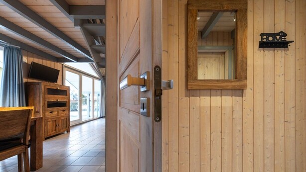 A wooden door with a mirror and a "HOME" sign, a wooden bench, and a TV on a wooden cabinet in a room with wooden walls and tiled flooring. - skandinavisches Ferienhaus in Mirow (Granzow)