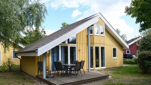 A yellow building with a sloped roof, large windows, and a wooden deck with outdoor furniture. - skandinavisches Ferienhaus in Mirow (Granzow)