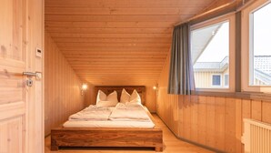 A wooden cabin bedroom with a bed, wooden walls, a window with curtains, and a radiator. - skandinavisches Ferienhaus in Mirow (Granzow)