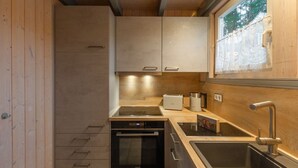 A compact kitchen with wooden cabinets, a built-in oven, a sink, and a window with a lace curtain. - skandinavisches Ferienhaus in Mirow (Granzow)