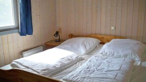 A single bed in a room with wooden walls and a window with a blue curtain.
