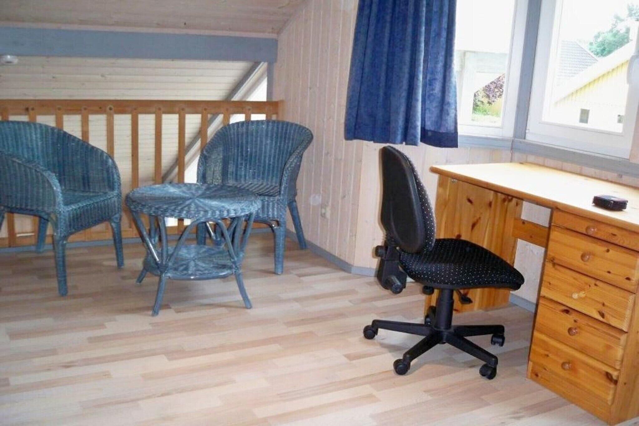 Ett rum med tre fåtöljer i rotting, en svart kontorsstol och ett skrivbord i trä med lådor.