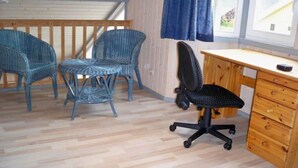 A room with three wicker chairs, a black office chair, and a wooden desk with drawers.