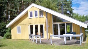 A yellow wooden house with a white roof, large windows, and a porch with chairs.