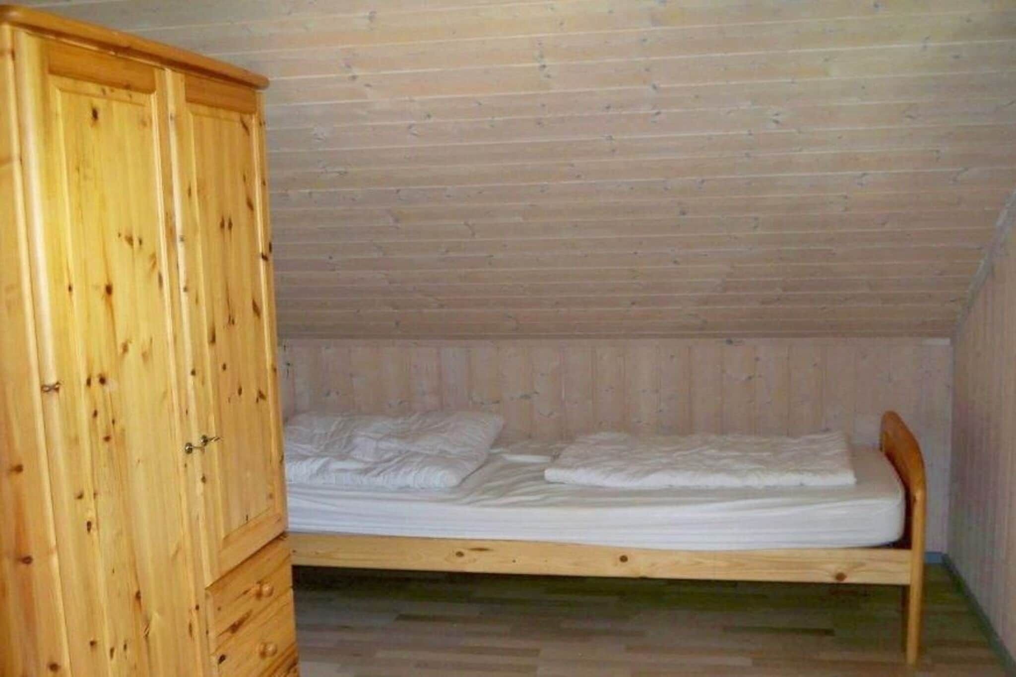 Habitación pequeña con cama individual, armario de madera y techo inclinado.