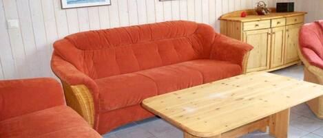 A room with a red sofa, a wooden coffee table, and a wooden cabinet with a microwave on top.