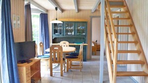 A wooden interior with a dining table, chairs, a TV, and a staircase.