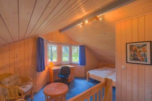 A cozy cabin room with a wooden interior, a desk, a chair, a bed, and a window with curtains. - Ferienhaus im Ferienpark Mirow (Granzow)