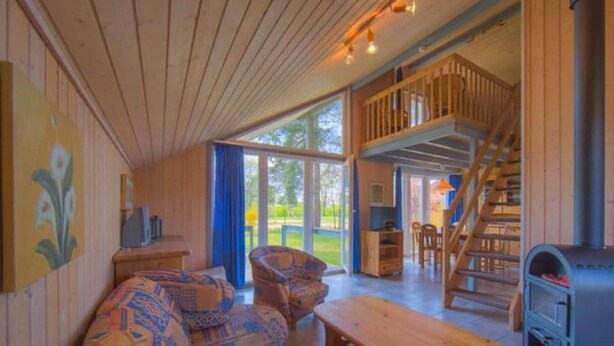 Un intérieur chaleureux avec un plafond en bois, un canapé, une table, une cheminée et un escalier menant à un niveau supérieur.