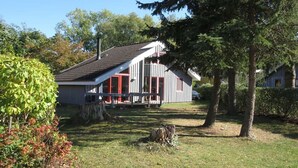 Una casa a un piano con tetto spiovente, un portico con ringhiere rosse e un camino.