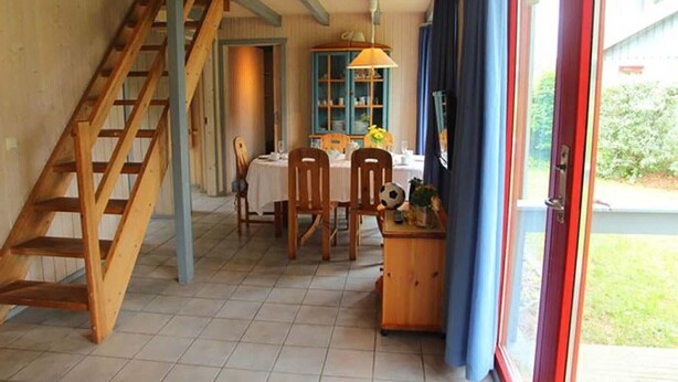 Zona pranzo con tavolo apparecchiato per due, una scala in legno e vista all'esterno tramite una porta in vetro.
