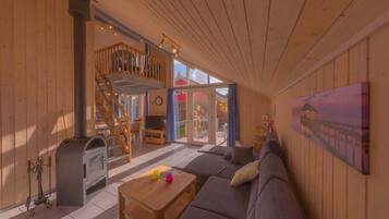 L’intérieur chaleureux d’un chalet, avec un revêtement mural en bois, un canapé, une table basse, une cheminée et un escalier menant à un étage supérieur.