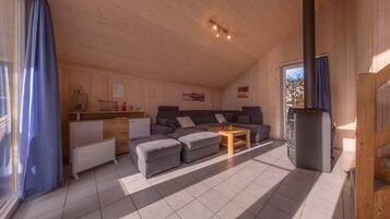 L’intérieur d’un chalet accueillant, avec un plafond en bois, un ensemble de canapés, une petite table et une cheminée.