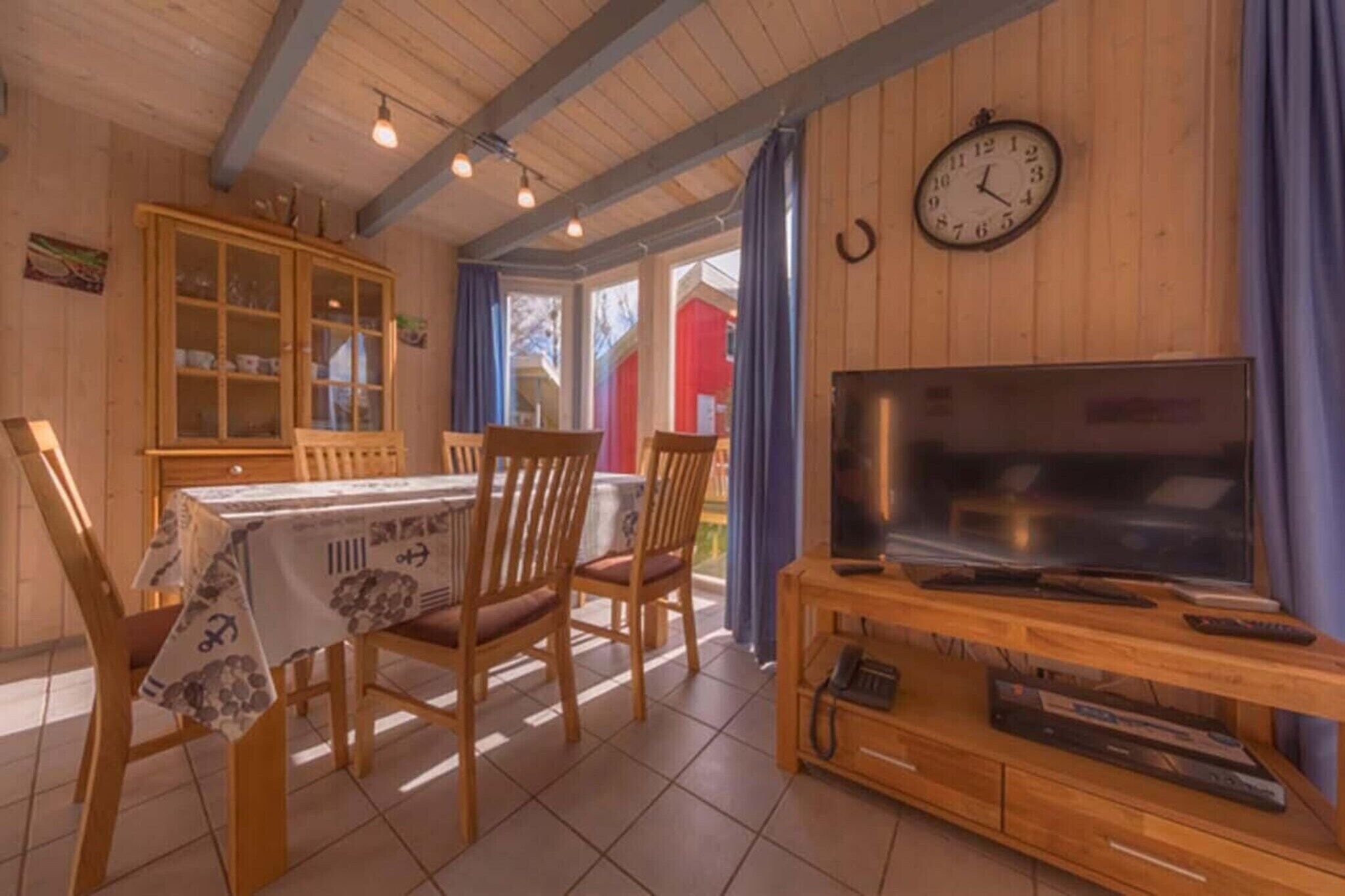 Puisesta materiaalista valmistettu ruokailutila, jossa on neljälle katettu ruokapöytä, puinen televisioteline ja seinällä oleva kello.
