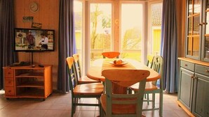 Un comedor con una mesa y sillas de madera, un televisor sobre un mueble bajo, y vistas amplias a través de grandes ventanas.