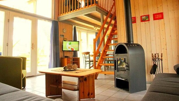 Un acogedor interior de cabaña con una mesa de comedor de madera, un sofá, un televisor, una chimenea y una escalera de madera.