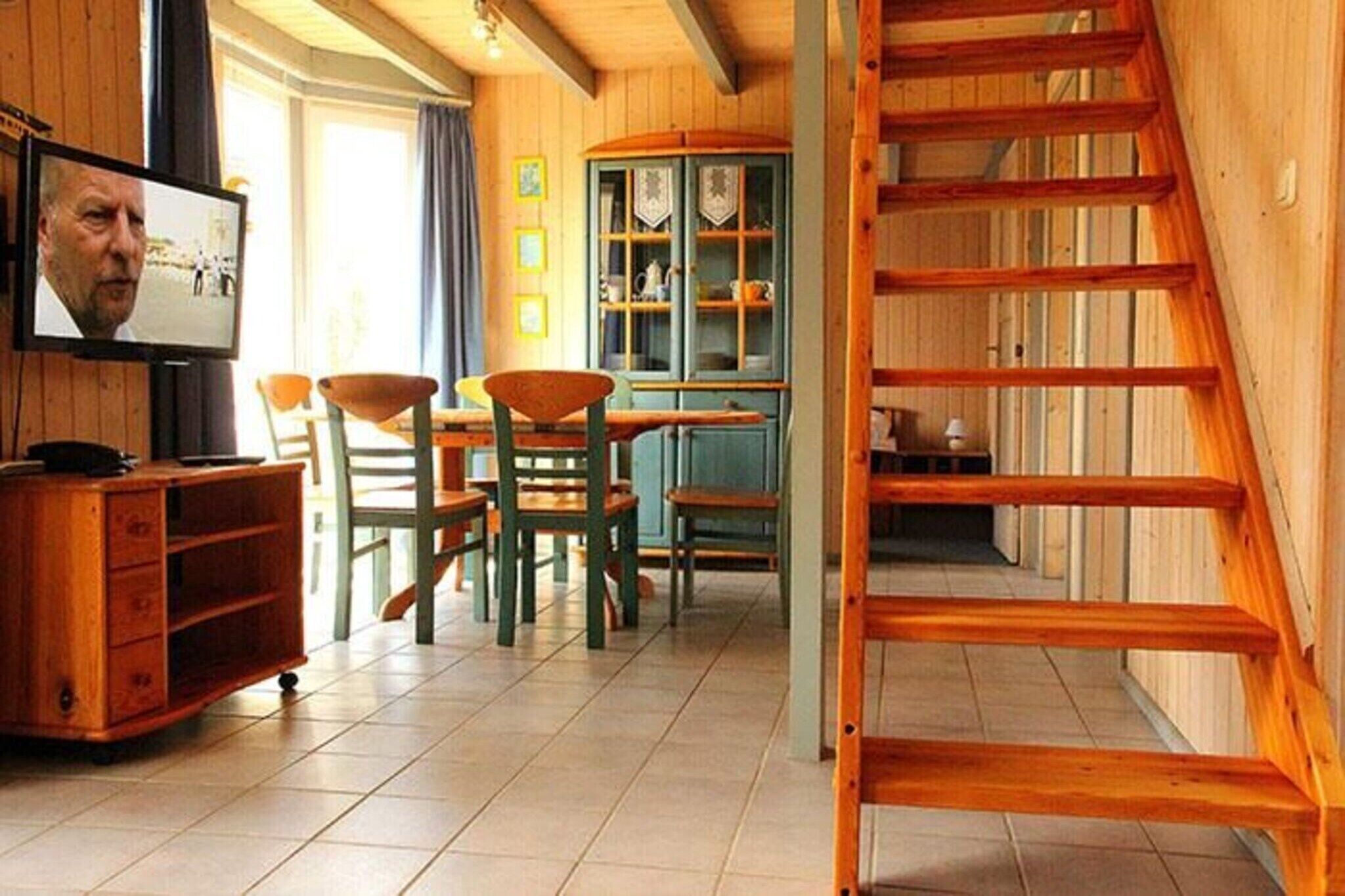 Un interior de madera con zona de comedor, televisor y escalera.