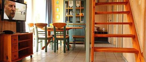 Un interior de madera con zona de comedor, televisor y escalera.