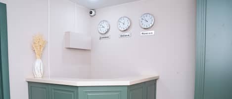 Una cocina con un mueble de color verde y una encimera blanca. Hay tres relojes en la pared etiquetados Londres, Astana y Moscú.