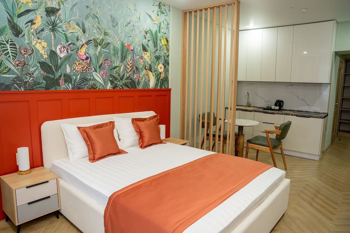 A hotel room with a bed, a nightstand, a desk, and a kitchenette.