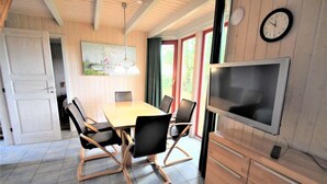 A dining area with a wooden table and chairs, a TV mounted on the wall, and a door leading to another room. - skandinavisches Ferienhaus in Mirow (Granzow)