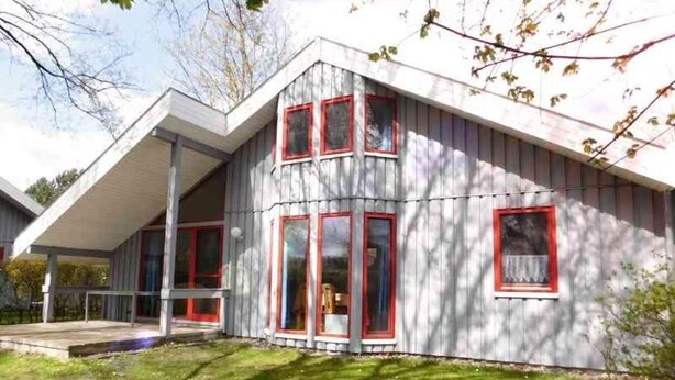 A modern two-story house with a sloped roof, large windows with red frames, and a covered porch area. - skandinavisches Ferienhaus in Mirow (Granzow)