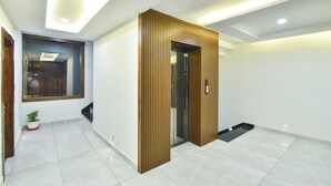 Un interno moderno con una parete d'accento in legno, un ascensore in vetro e un pavimento piastrellato.