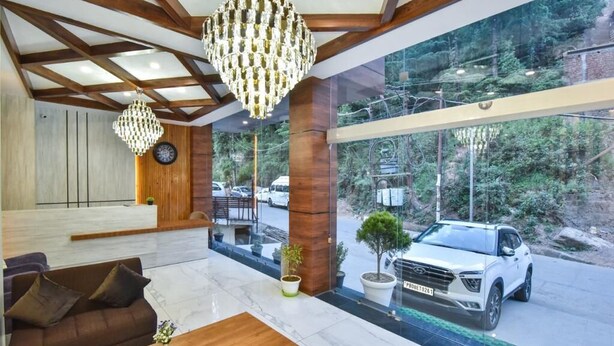 Una hall moderna con travi in legno, un lampadario, la reception, un’area salotto e vista su un SUV bianco in strada.