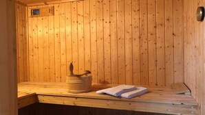 A wooden sauna with a bench, a wooden bucket, and a folded towel.