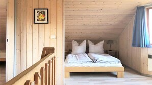 A wooden room with a bed, a framed picture on the wall, and a window with curtains.