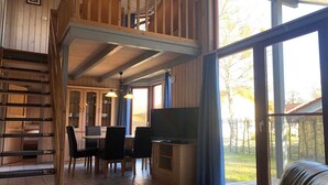 A wooden interior with a dining area, a TV, and large windows.