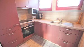 A compact kitchen with pink cabinets, a microwave, a coffee maker, and a sink.