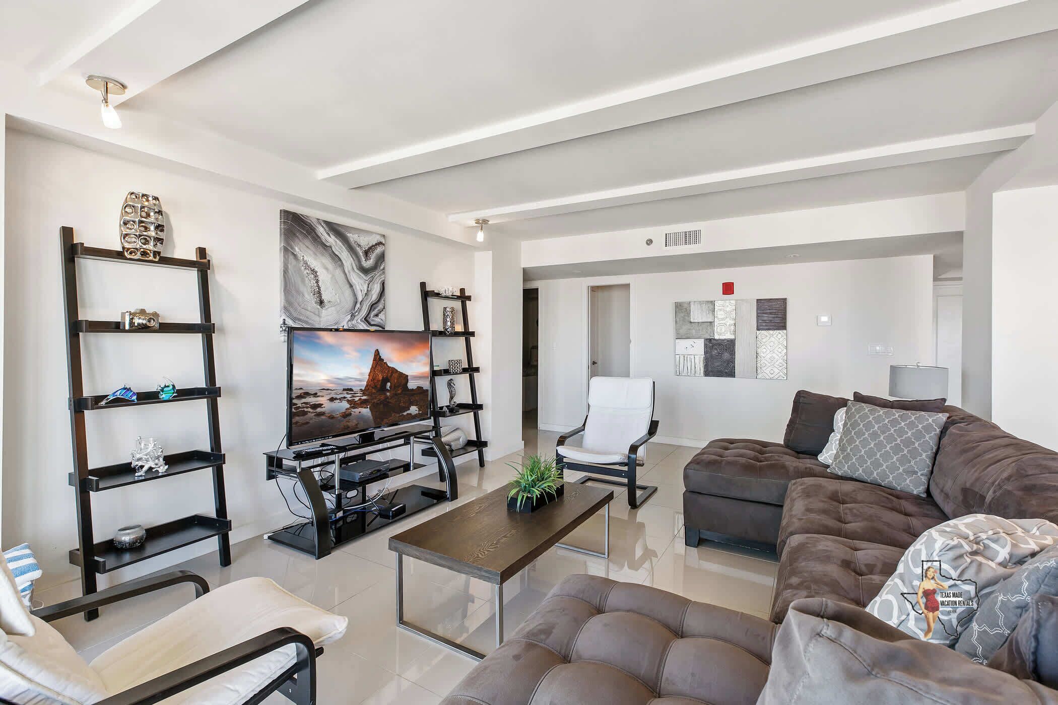 A modern living room with a flat-screen TV, a sofa, a coffee table, and a chair.