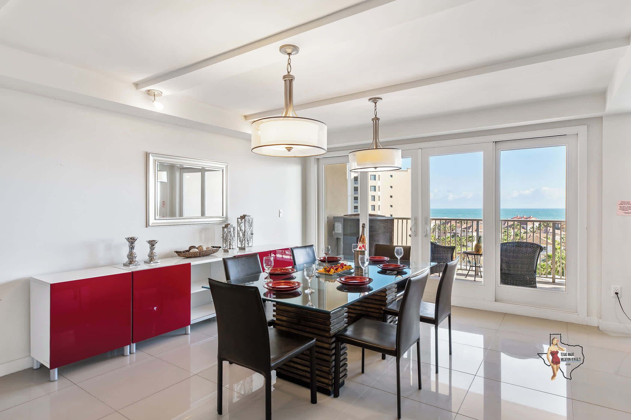 A modern dining area with a glass table, red and white cabinet, and a balcony with a view.