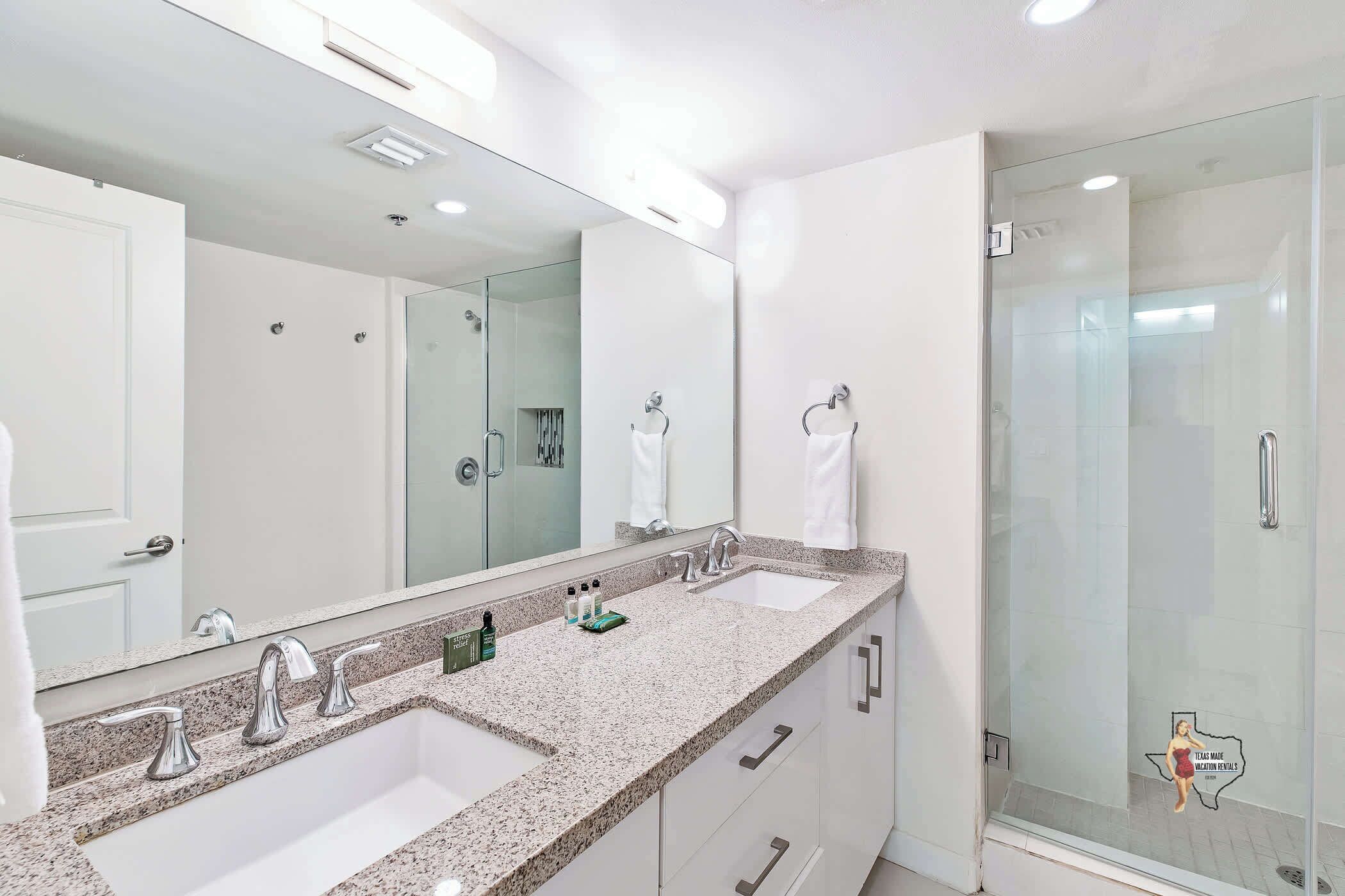 A modern bathroom with two sinks, a large mirror, and a glass shower enclosure.