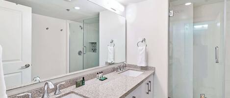 A modern bathroom with two sinks, a large mirror, and a glass shower enclosure.