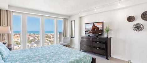 A bedroom with a large bed, a TV, a dresser, and a view of the sea.