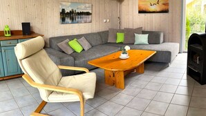 Ein gemütliches Wohnzimmer mit einem grauen Ecksofa, einem Holztisch und einem cremefarbenen Schaukelstuhl.