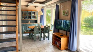 Ein gemütliches Zimmer mit einer Holztreppe, einem Esstisch mit Stühlen, einem Fernseher und einem Bücherregal.