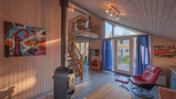Un vaste espace de vie doté d’un plancher en bois, d’une cheminée, d’un balcon et d’une grande fenêtre.