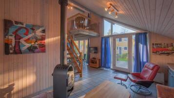 A spacious living area with a wooden floor, a fireplace, a balcony, and a large window.