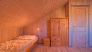 Une pièce aux murs et au plafond en bois, un lit simple avec un matelas blanc, une armoire en bois et une porte.