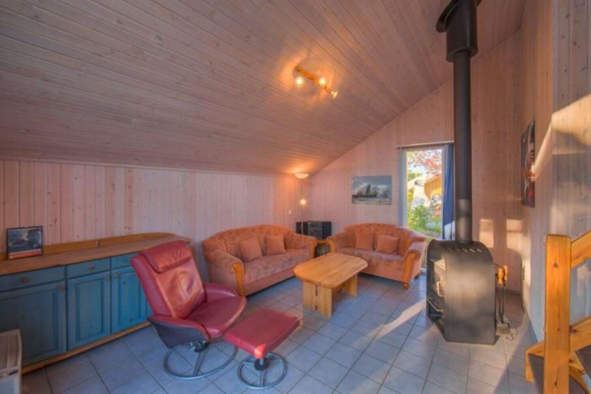 A cozy cabin interior with wooden walls, a sofa, a chair, a table, and a wood-burning stove.