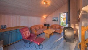 L’intérieur d’un chalet chaleureux, avec des murs en bois, un canapé, un fauteuil, une table et un poêle à bois.