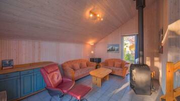 A cozy cabin interior with wooden walls, a sofa, a chair, a table, and a wood-burning stove.