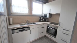 A compact kitchen with white cabinets, a dishwasher, a stove, and a microwave. - skandinavisches Ferienhaus in Mirow (Granzow)